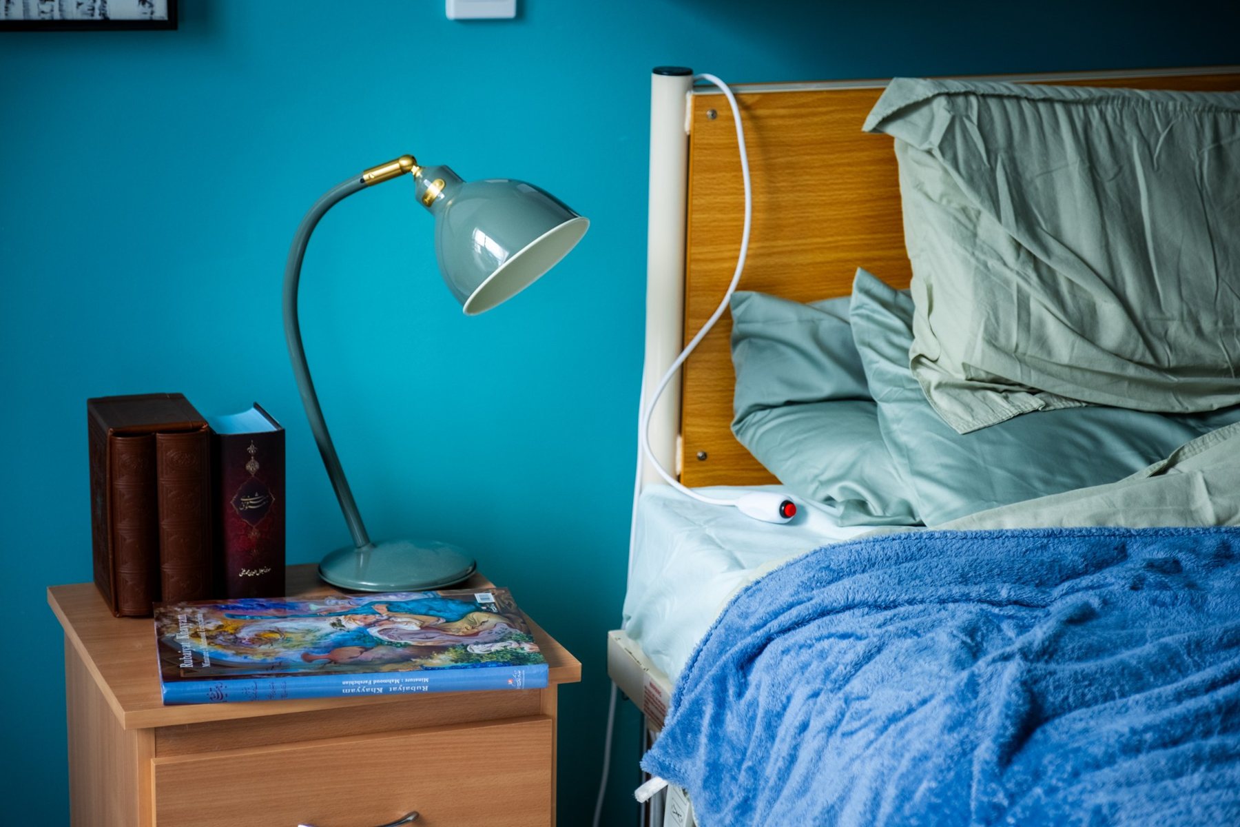 Bedroom set photograph from Sing Me to My Death, with a bedside lamp against a teal wall